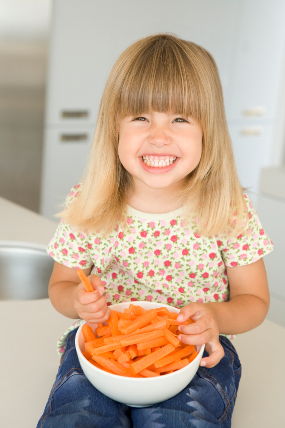 Young girl in kitchen eating carrot sticks smiling